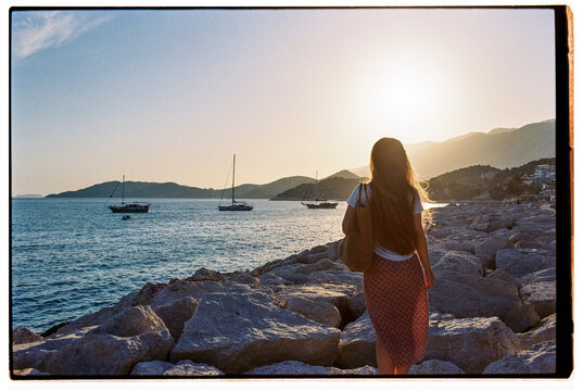 Anonymous woman standing at the seashore watching yachts passing by