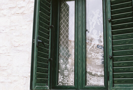 Green wooden window shutters frame delicate lace curtains 