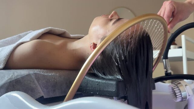Close-up of a woman receiving a head massage during a Japanese head spa treatment with water flowing from a special hair washing tool, focusing on the scalp relaxation and beauty therapy