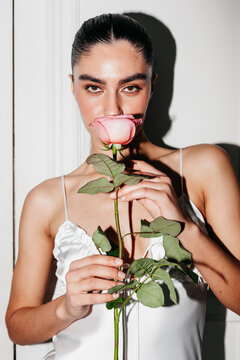 Portrait of a woman holding a pink rose near a wall