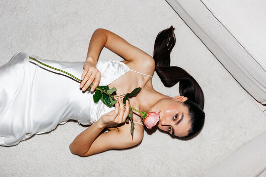 Woman in elegant dress lying on soft rug holding a rose