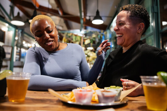 Two Friends Laughing and Enjoying Drinks at a Cozy Restaurant Table
