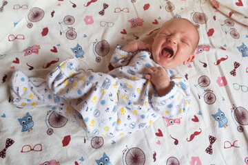 A newborn baby screams and cries on the bed