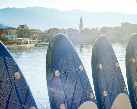 Sapboards stand in a row against the backdrop of the city of Budva