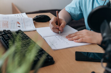 Teen boy studying at home on desktop computer. Focused child in headphones attending online class,...