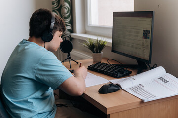 Teen boy studying at home on desktop computer. Focused child in headphones attending online class,...