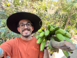 A happy man is carrying a bunch of green bananas