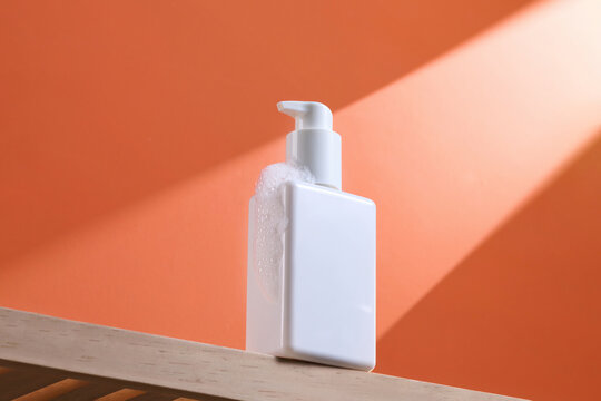 A white soap dispenser with foam rests on a wooden shelf