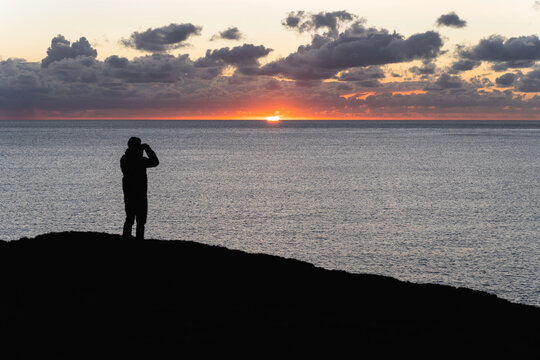 A person observing with binoculars a majestic sunset by the sea