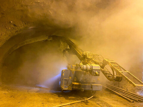 Underground Mining Tunnel with Machine Excavating in Dust and Lighting