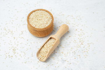 Sesame seeds in wooden bowl and scoop on white surface
