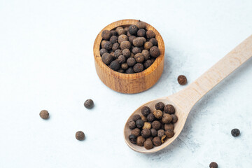 Whole black peppercorns in a wooden bowl and spoon on a light background