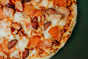 Pizza topped with pepperoni and ham on a green surface ready to enjoy