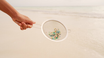Sieve with plastic particles on beach, microplastic pollution, ocean contamination, beach debris,...