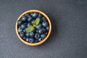Fresh blueberries in a wooden bowl on a dark textured surface