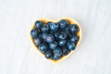 Fresh blueberries in a heart-shaped bowl on a light background