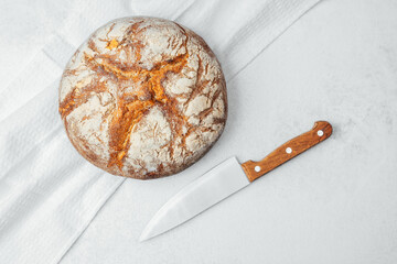 Freshly baked round loaf of bread with a knife on a light kitchen surface