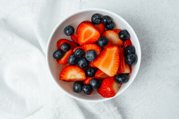 Fresh strawberries and blueberries in a bowl on a light surface