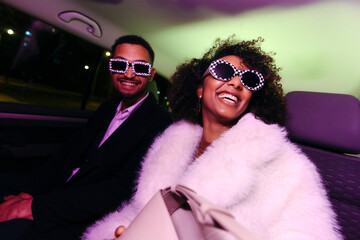 Happy glamorous couple inside car going out to a party at night