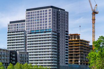 Fototapeta premium Modern residential and office buildings under construction in the city center. Tall skyscrapers, a construction crane, and elements of contemporary architecture create a dynamic urban landscape.