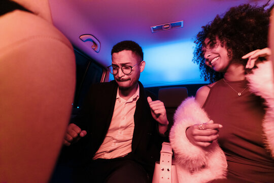 Two friends dancing to music inside a car with colorful lights