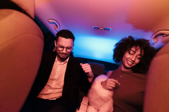 Two friends dancing to music inside a car with colorful lights