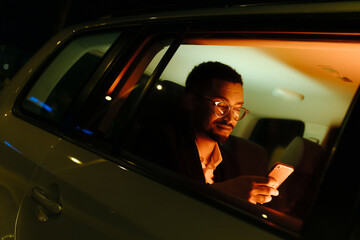 Portrait of man browsing his phone inside a car at night
