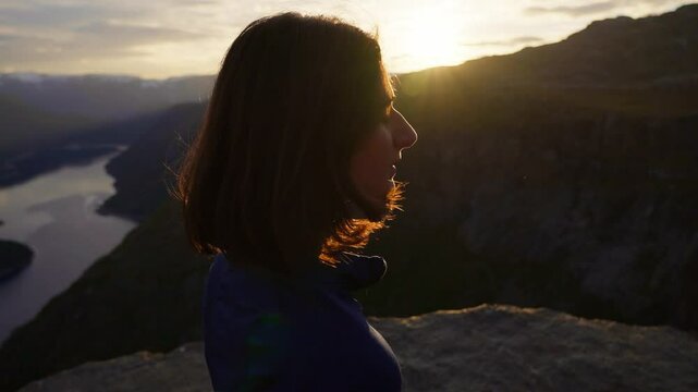 Woman looking at a river valley during sunset in Norway, peaceful and thoughtful moment, Trolltunga