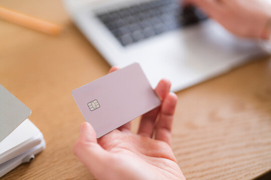 A person holds a credit card while using a laptop. They are possibly making an online purchase or managing their finances.
