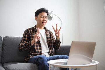 Happy joyful casual man learning and communicates in sign language online at a laptop at cozy home
