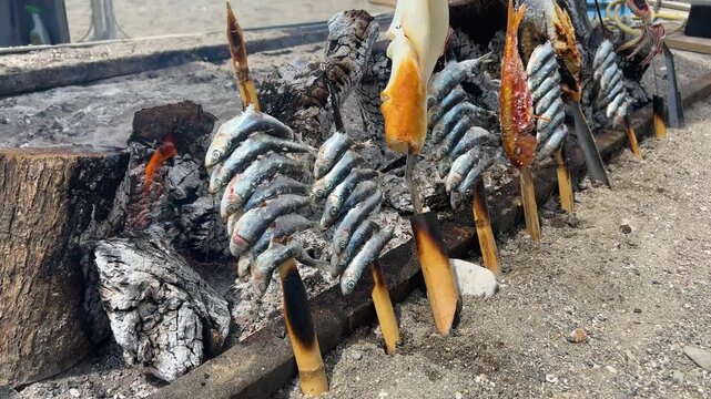 Fishmonger grilling fresh sardines on skewers over hot coals, a traditional seafood cooking method. Typical "espetos" food of Spain, Costa del Sol, Malaga.
