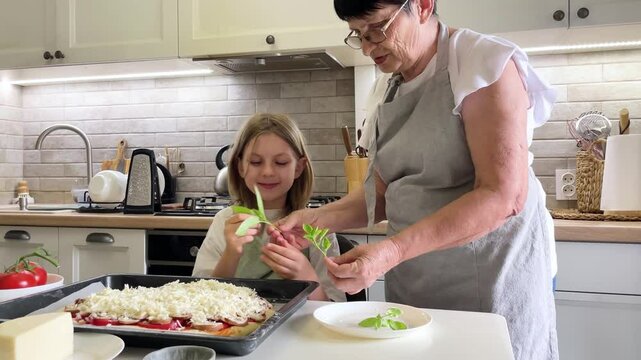Grandmother and granddaughter adding basil leaves to pizza