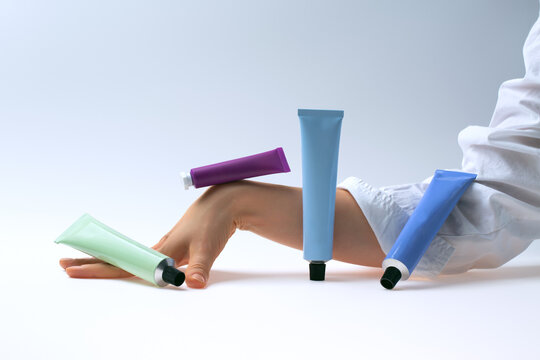 Multicolored tubes of cream balanced on hand against light background