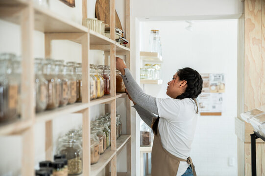 Worker Organizing Jars on Wooden Shelves in Shop