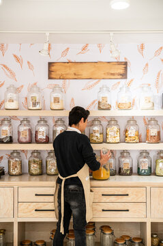 Shopkeeper organizes spices and dried goods on rustic shelves
