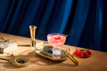 A glamorous pink cocktail with cherries and elegant gold bar tools