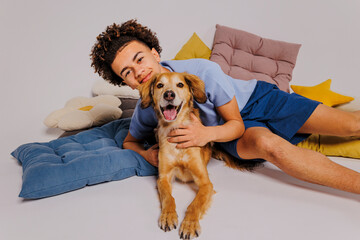 Happy teenager hugging his dog on floor with colorful cushions