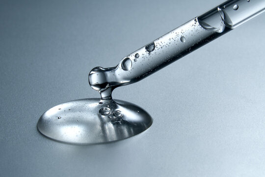 Clear glass pipette with a drop of cosmetic product falling down. 