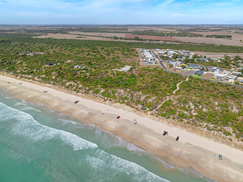 4x4s parked on a long sandy beach nea r coastal town
