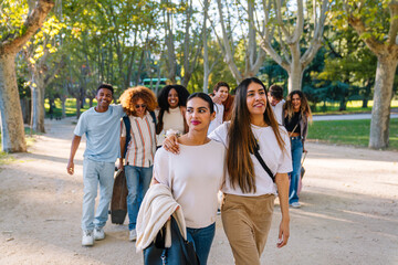 Group of multi ethnic students walking and chatting joyfully in a sunny park, enjoying friendship...