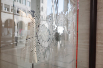 Close-up of cracked storefront window with central impact point, surrounded by red caution tape....