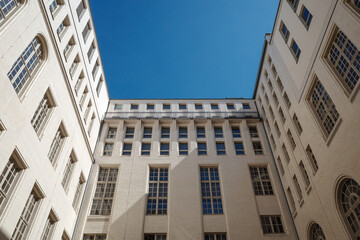 Fototapeta premium The geometric symmetry of tall white brick buildings forming an enclosed courtyard, with a clear blue sky visible above.