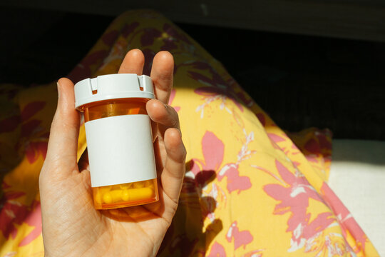 Hand Holding Medicine Bottle with Pills and Blank Label