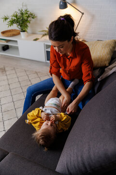 woman changing diaper of daughter on sofa at home