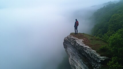 Hiker on misty clifftop, overlooking valley. Travel stock photo