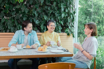 Caucasian man and senior Asian man chatting with smiling woman at cafe table. Hot beverages, pastries, and relaxed interaction reflect casual lifestyle, senior, chatting, cafe, leisure, friends.