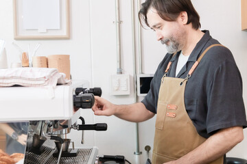 Senior entrepreneur prepares coffee with steady hands, dressed in apron. cafe professtional bar reflects a small business owner identity hard work, skill, freedom retired occupation working lifestyle