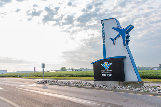 Waterloo, CANADA - Aug 5 2024 : Large entrance sign for Region of Waterloo International Airport with airplane symbol, located beside a rural road under cloudy skies.