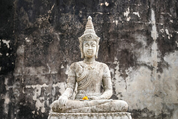 Stone Buddha statue in meditation pose against old ruined wall