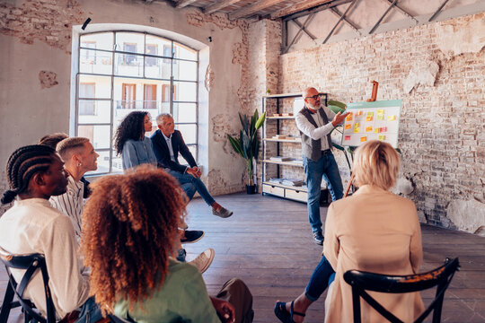 Senior manager using kanban board presenting business strategy to diverse team in loft office